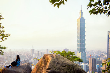 Fototapeta premium Taipei, Taiwan - January 25, 2019: tourist woman sit on giant stone with 101 tower at sunset