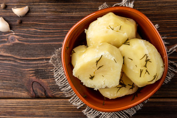 Boiled potato in brown bowl on dark wooden background.