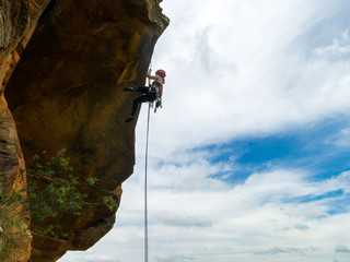 Abseiling a negative sanstone rock wall with blue sky on background