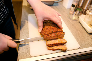 Woman hands cutting piece of meatloaf, she prepare for tasting of food at kitchen. Chef cutting meatloaf with knife on board on restaurant kitchen table. Housewife sliced meatloaf on cutting board.