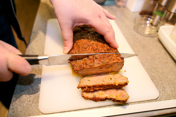 Woman hands cutting piece of meatloaf, she prepare for tasting of food at kitchen. Chef cutting meatloaf with knife on board on restaurant kitchen table. Housewife sliced meatloaf on cutting board.