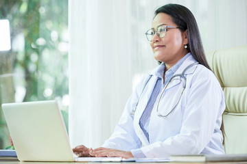 Positive doctor working on laptop