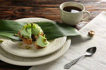 Tasty pistachio tartlet with cup of tea on table