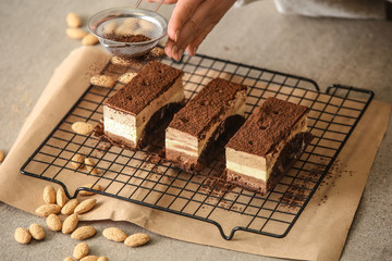 Female confectioner sprinkling cacao powder onto tasty cakes at table