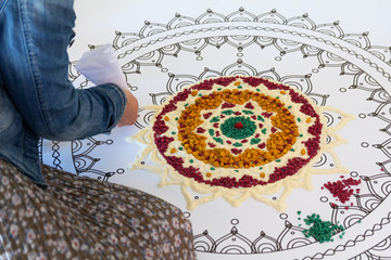 Girl creating a mandala by means of color sand. Religion