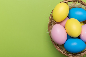 Colorfull easter eggs in nest on green pastel color background with space.