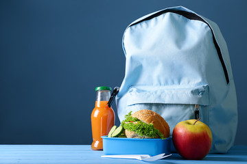 Schoolbag and lunch box with healthy food on table