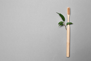 Wooden toothbrush and green leaves on grey background. Ecology concept