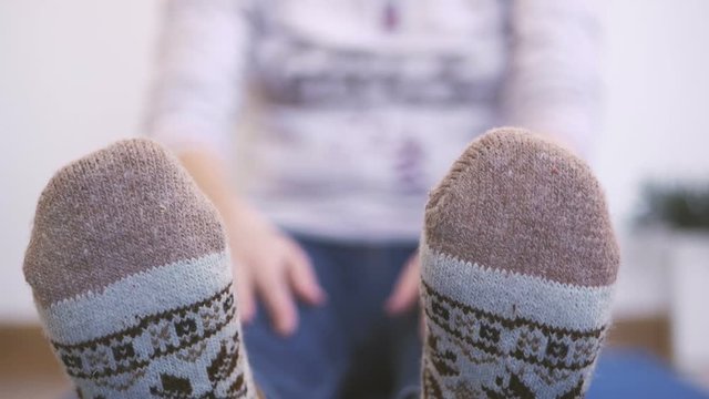 A woman in warm knitted socks does morning exercises, while sitting stretches her fingers up to her toes.