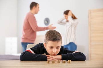 Sad little boy with coins and his quarreling parents at home. Concept of child support