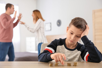 Sad little boy with coins and his quarreling parents at home. Concept of child support