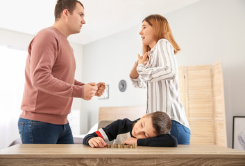 Sad little boy with coins and his quarreling parents at home. Concept of child support