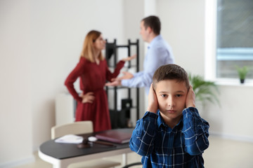 Sad little boy with his quarreling parents in lawyer's office. Concept of child support
