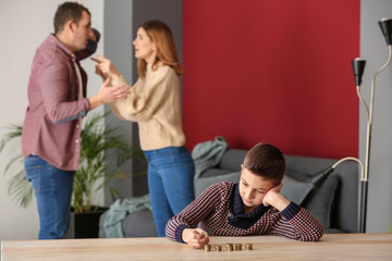 Sad little boy with coins and his quarreling parents at home. Concept of child support