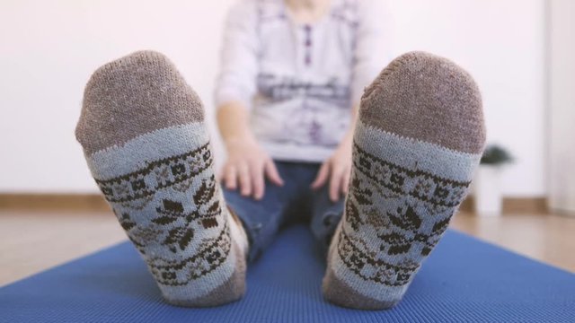 A woman in warm knitted socks does morning exercises, while sitting stretches her fingers up to her toes.
