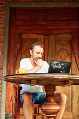 Man with smartphone, coffee / tea and laptop on a home porch.