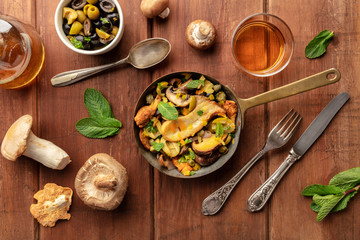 An overhead photo of a rustic mushrooms and olives saute with mint, with a glass of white wine