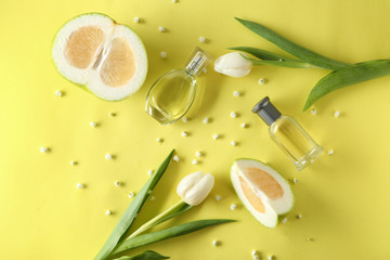 Bottles of perfume, flowers and citrus fruit on color background