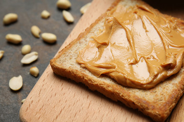 Wooden board with toasted bread and tasty peanut butter on grey background, closeup