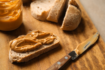 Fresh bread with peanut butter on wooden board, closeup