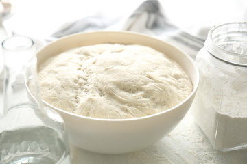 Bowl with fresh dough for bread on light table