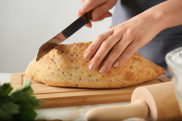 Young woman cutting fresh bread at table, closeup