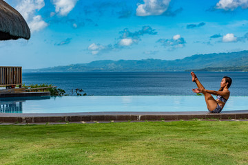 Filipina girl doing yoga poses poolside with ocean background