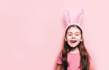 Easter girl portrait. Cute little girl with bunny ears on pink background. Easter child portrait, funny emotions, surprise. Copyspace for text.