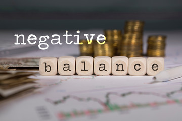 Term NEGATIVE BALANCE composed of wooden letters. Stacks of coins in the background.