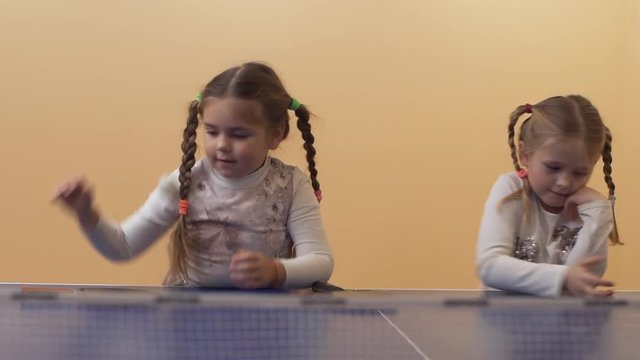 Two pretty little girls with braided pigtails playing with table tennis balls. Leisure of happy sisters. Slow motion.