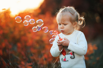 Little girl blowing soap bubbles in autumn park at sunset. Happy childhood concept. - Image
