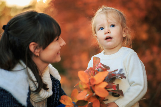 Mother and daughter with fallen leaves in autumn park. Little girl and her mom playing in the garden. - Image