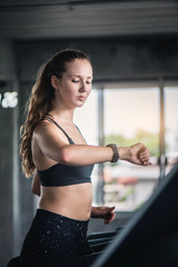 Attractive pretty Caucasian woman running on treadmill and check heart rate with smart watch at gym. 