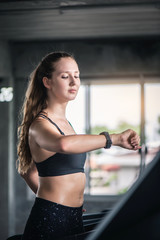 Fototapeta na wymiar Attractive pretty Caucasian woman running on treadmill and check heart rate with smart watch at gym. 