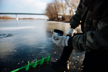 Fisherman drinking tea from a thermos in the winter on the ice. Winter fishing