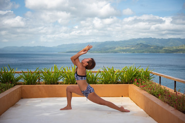 Filipina girl doing yoga poses poolside with ocean background