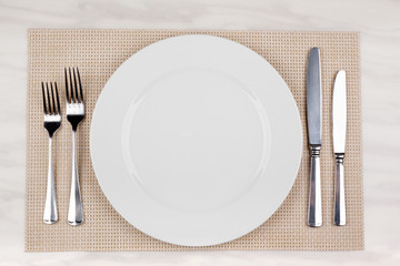 Empty white plate with cutlery is on the table. Knives and forks on both sides of the dishes.
