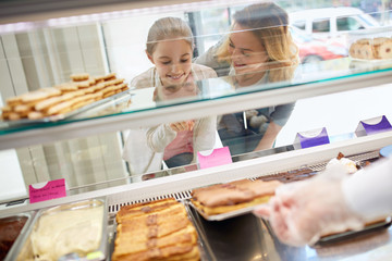 Girl with mother look at cookies in pastry shop.