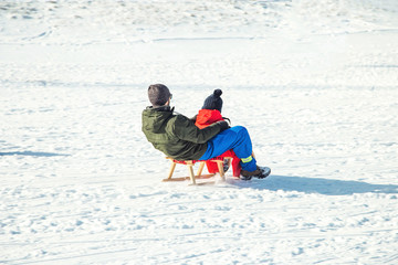 Fototapeta na wymiar Happy father and his son enjoying sledding ride. Happy family with sled in winter having fun together. Fast ride. Family driving sled under winter snow. Winter holidays.