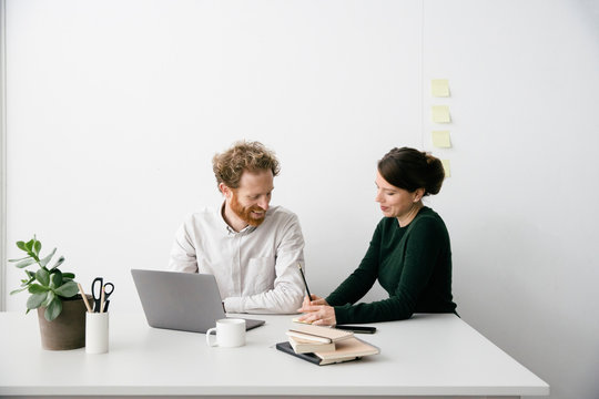 A thirty something couple is working on a laptop in a clean white empty office setting.