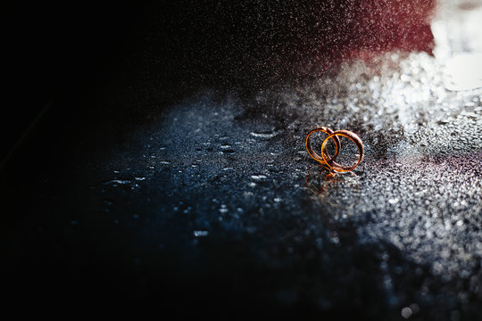 Wedding rings on dark surface shining with light close up macro. Water splashes. Reflection. Lights and smoke.