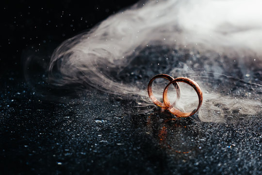 Wedding rings on dark surface shining with light close up macro. Water splashes. Reflection. Lights and smoke.