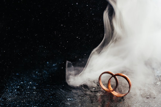 Wedding rings on dark surface shining with light close up macro. Water splashes. Reflection. Lights and smoke.