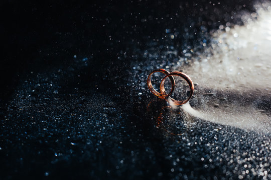 Wedding rings on dark surface shining with light close up macro. Water splashes. Reflection. Lights and smoke.