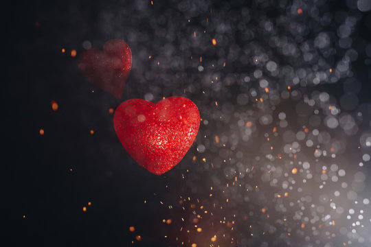 Two hearts are floating on a black background in the splash and the light. Valentine's day