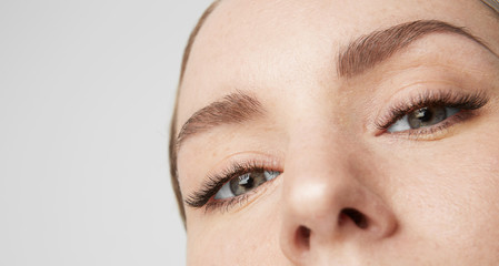 Close-up portrait Beauty female model with big blue eyes and dark eyebrows looking at camera.Model with light nude make-up, gray studio background