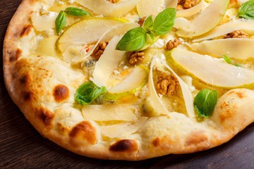 Vegetarian Italian pizza with nuts, yellow pear, parmesan cheese and fresh green basil leaves on a brown table decorated by basil leaves. Top view. Close up.
