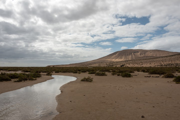 Small, natural brook on Sotavento beach, Costa Calma, Fuerteventura, Spain. Hills in the backgrund. 