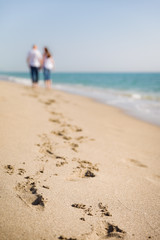 Young man and woman walking along the beach. Honeymoon. Footprints on the ocean beach. Selective focus