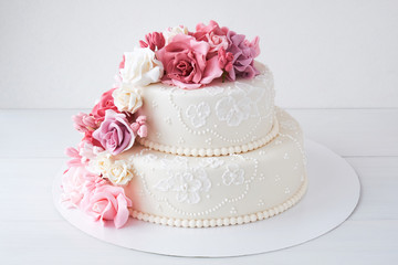 Obraz na płótnie Canvas Two-tiered white wedding cake decorated with pink flowers on a white wooden background.